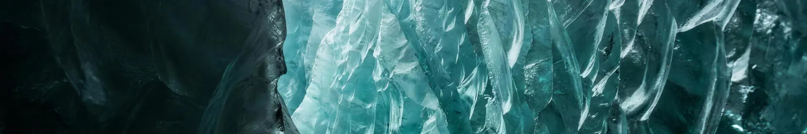 The crystalline teal wall of a glacier crevasse, angular fracture planes lit from within the ice