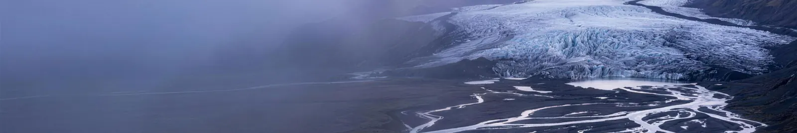A braided glacial river delta at dawn, dozens of silver meltwater channels weaving across dark gravel flats