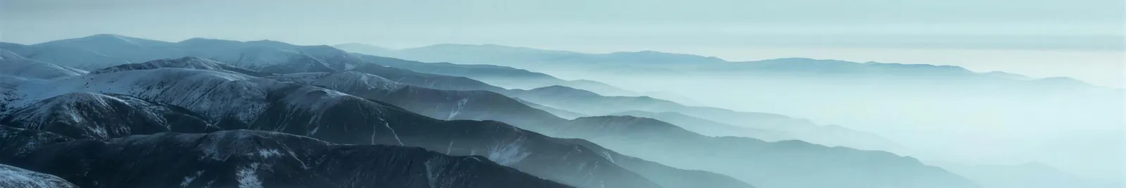 Rank after rank of mountain ridgelines receding into pale haze at blue hour